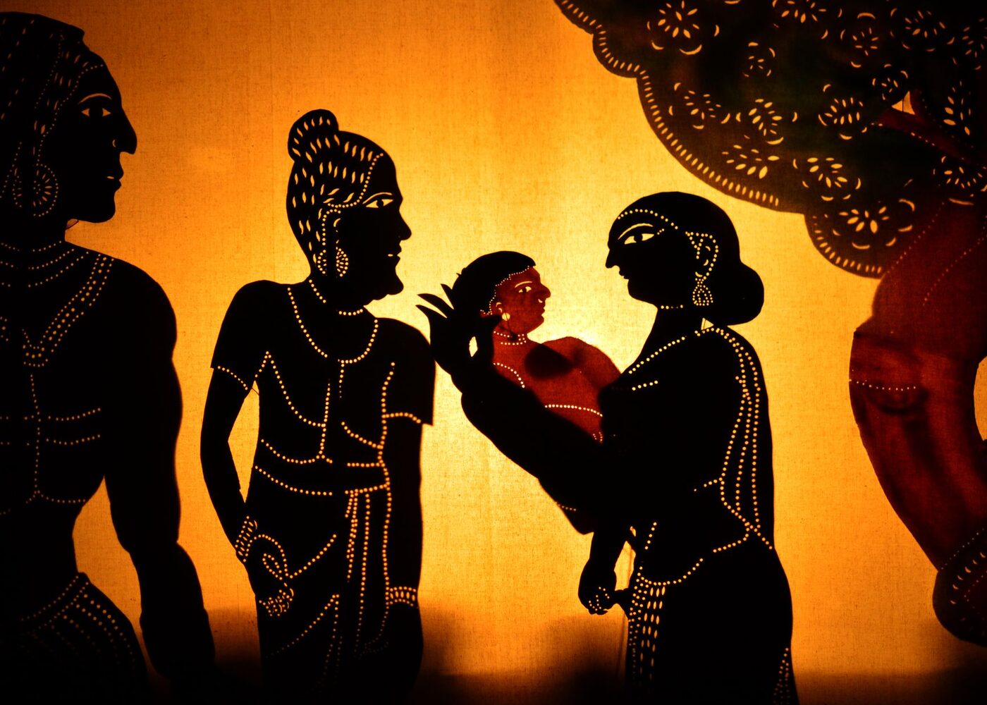पर्दे के पीछे एक दृश्य प्रस्तुत करती जलती हुई चमड़े की छाया-कठपुतलियाँ